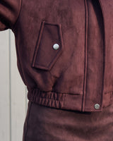 Close-up of the bomber jacket's press-stud flap pocket and elasticated hem in burgundy suede-look fabric