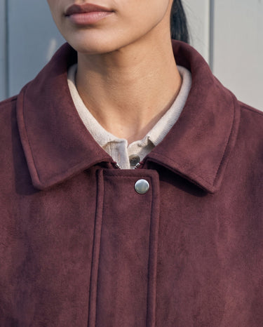 Close-up of the burgundy bomber jacket's spread collar and press-stud placket