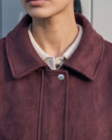 Close-up of the burgundy bomber jacket's spread collar and press-stud placket