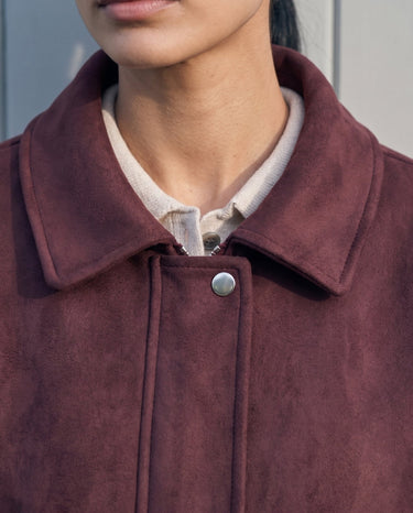 Close-up of the burgundy bomber jacket's spread collar and press-stud placket