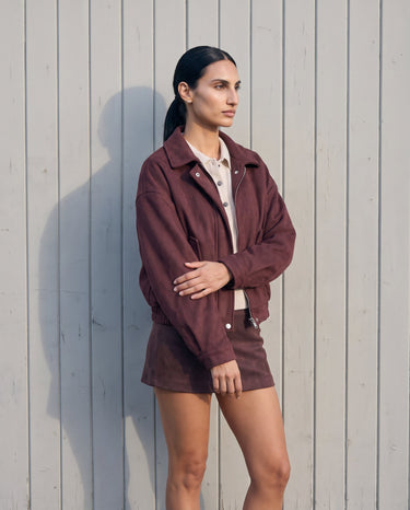 Model standing in the burgundy suede-look bomber jacket styled with a matching mini skirt, side-front view