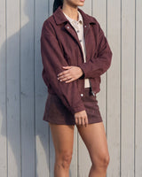 Model standing in the burgundy suede-look bomber jacket styled with a matching mini skirt, side-front view