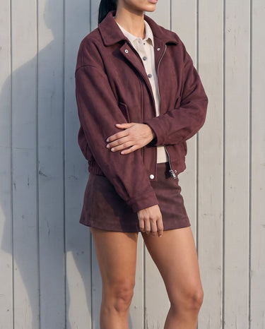 Model standing in the burgundy suede-look bomber jacket styled with a matching mini skirt, side-front view