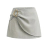The Ainsley Buckle Skort in light sage gray — wrap-front skort with gold ring buckle, product flat-lay