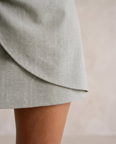 The Ainsley Buckle Skort in light sage gray — close-up of the wrap-front overlay and hem