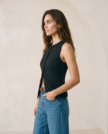 The Alicia vest in black — front three-quarter view with hand in pocket on model