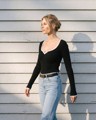 Model wearing the black ribbed knit top against a white clapboard wall, front view – Moriel Heritage