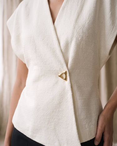 The Asymmetrical Vest in white — close-up of the V wrap neckline and gold button closure