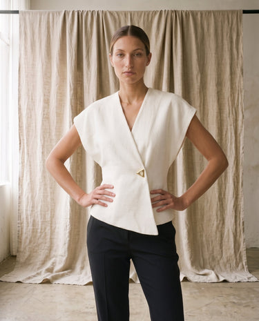 The Asymmetrical Vest in white — sleeveless vest with drop shoulders, front view on model with hands on hips