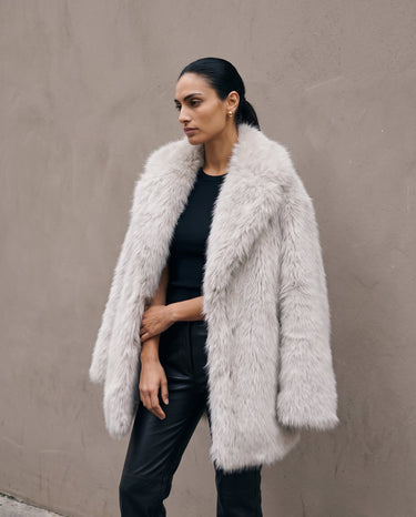 Model wearing the light gray Ballerina Faux Fur Coat open over a black top and black leather-look trousers, side view