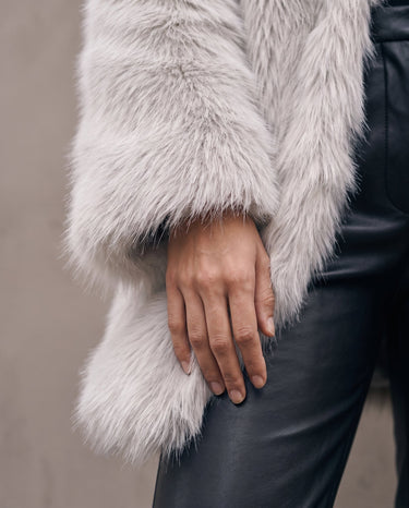 Detail of the Ballerina Faux Fur Coat's sleeve and hem over black trousers