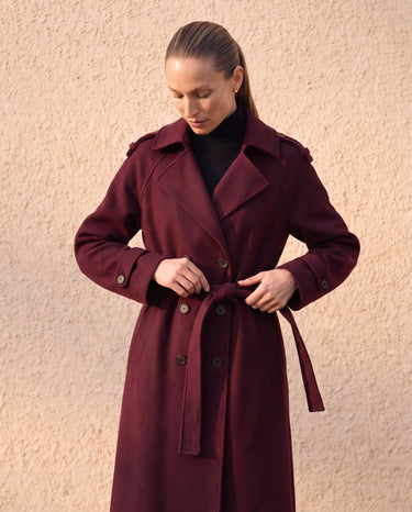 The Burgundy Celine Coat in burgundy — front view on model tying the belt
