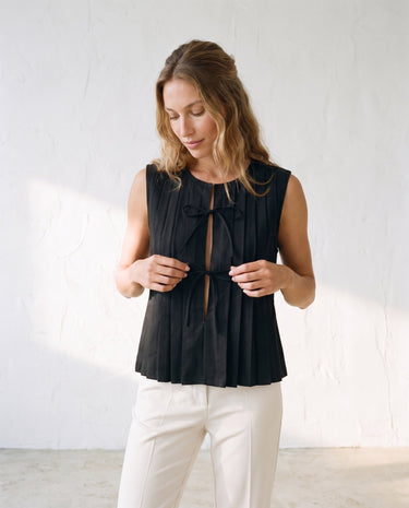 The Cala Cotton Linen Tie Top in black — pleated sleeveless tie-front top, front view on model