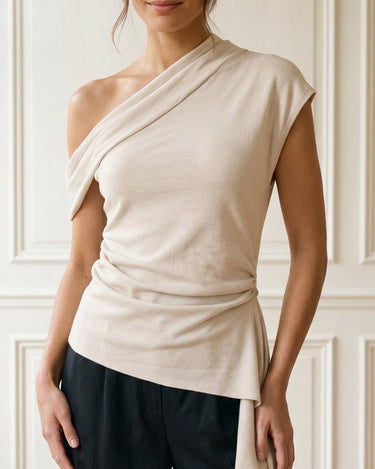 The Camellia Ruffle Top in beige — asymmetric one-shoulder top with draped ruffle, front view on model