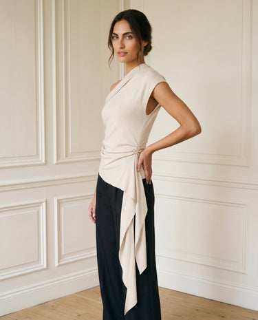 The Camellia Ruffle Top in beige — one-shoulder top with cascading side ruffle, side view on model