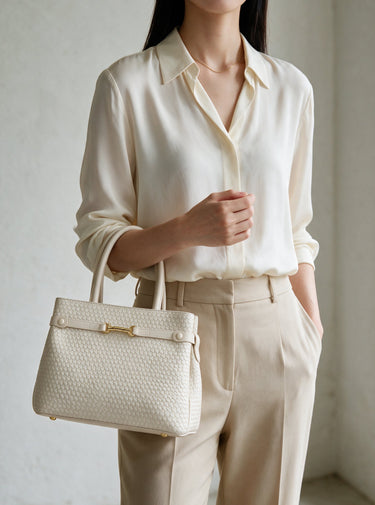 The Camille Handbag in ivory carried by hand with a cream shirt and beige trousers