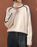 Model wearing cream high-neck knit sweater with black contrast piping and lantern sleeves, front view – Moriel Heritage