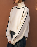 Model wearing cream high-neck knit sweater with grey trousers, three-quarter side view – Moriel Heritage
