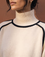 Close-up of cream knit sweater showing ribbed high neck and black piping across the shoulders – Moriel Heritage