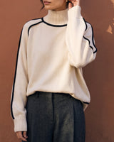 Model wearing cream high-neck knit sweater with hand to ear, front view – Moriel Heritage