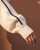 Close-up of cream sweater sleeve showing black piping and ribbed cuff – Moriel Heritage