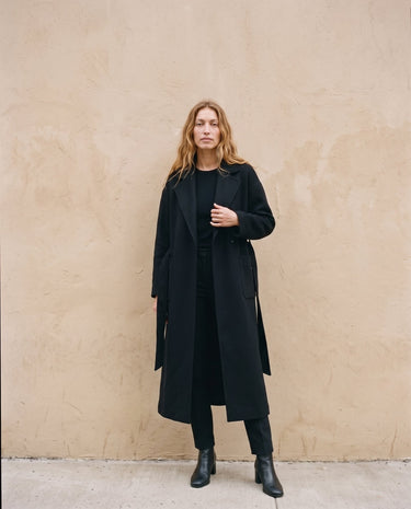 The Caroline Tie Waist Coat in black — longline belted coat worn open, front view on model
