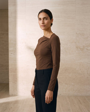 The Celeste Asymmetrical Long Sleeve Top in coffee — asymmetric-neck long-sleeve top, three-quarter view on model