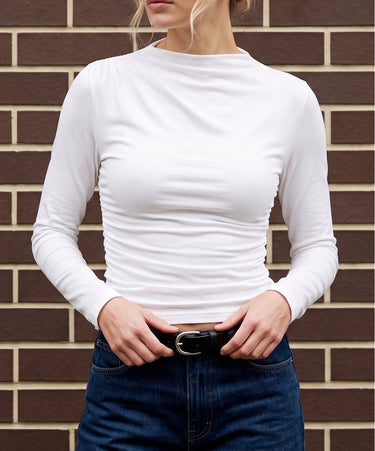 Model wearing white ruched long-sleeve top with dark jeans and a black belt, cropped front view – Moriel Heritage