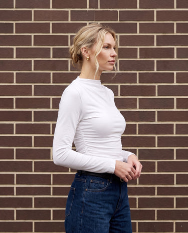 Model wearing white ruched long-sleeve top, side view showing gathered side seam – Moriel Heritage