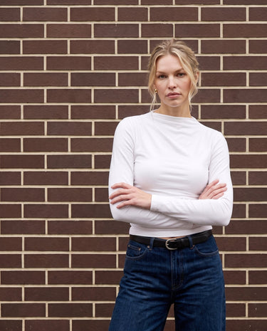 Model wearing white ruched long-sleeve top with arms crossed, front view – Moriel Heritage