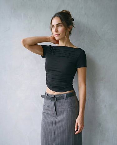 Model wearing black boat-neck top, hand to neck, three-quarter front view – Moriel Heritage