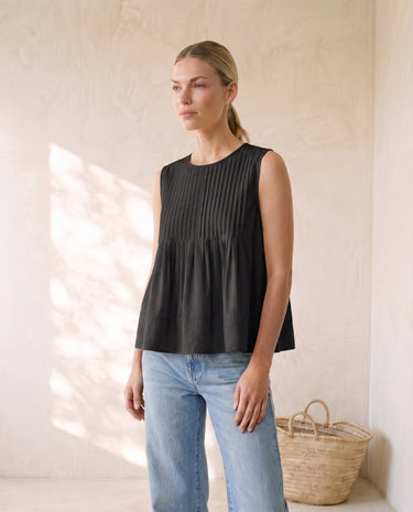 The Elio Pleat Vest in black — sleeveless pleated swing top, front view on model
