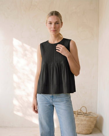 The Elio Pleat Vest in black — sleeveless pleated swing top, front view on model