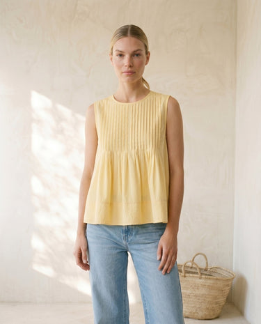 The Elio Pleat Vest in yellow — sleeveless pleated swing top, front view on model