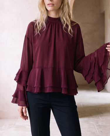 The Eloise Ruffle Blouse in burgundy — high-neck ruffle-sleeve blouse, front view on model
