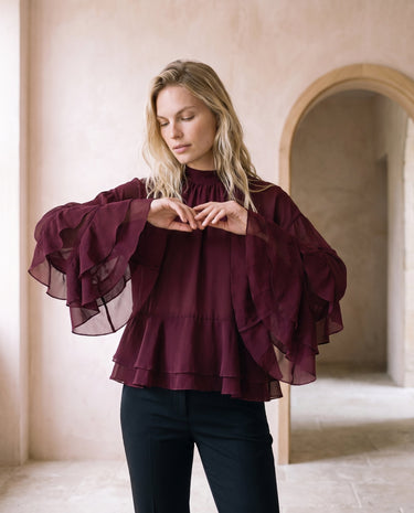 The Eloise Ruffle Blouse in burgundy — tiered ruffle-sleeve blouse, front view on model