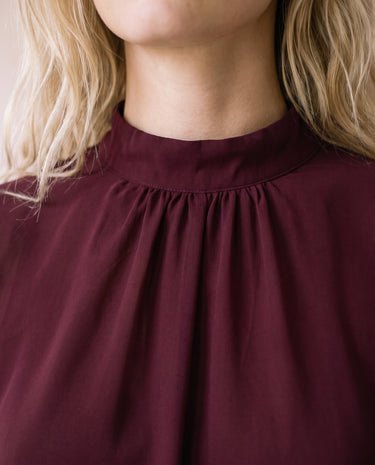 The Eloise Ruffle Blouse in burgundy — close-up of gathered high neckline