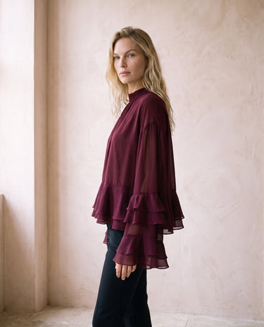 The Eloise Ruffle Blouse in burgundy — ruffle-sleeve blouse, side view on model