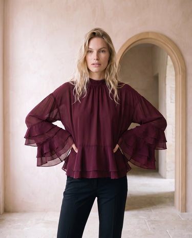 The Eloise Ruffle Blouse in burgundy — high-neck ruffle-sleeve blouse, front styling view on model