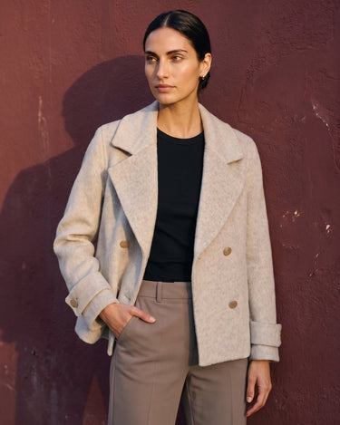 The Georgia Wool Coat in beige — double-breasted coat, front view with hand in pocket on model