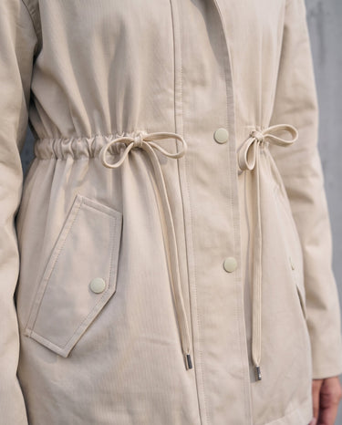 Close-up of the Halden Coat's drawstring waist, press-stud placket and slanted welt pocket in light khaki