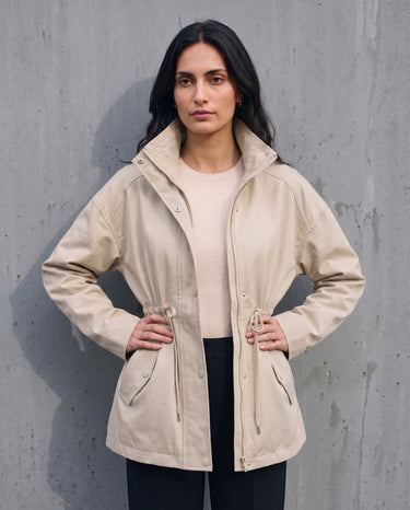 Model in the light khaki Halden Coat over a cream top and black trousers, front view