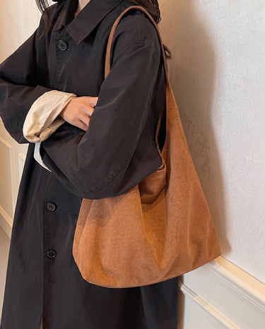 The Léa Slouch Tote in brown suede carried over the shoulder with a dark brown coat