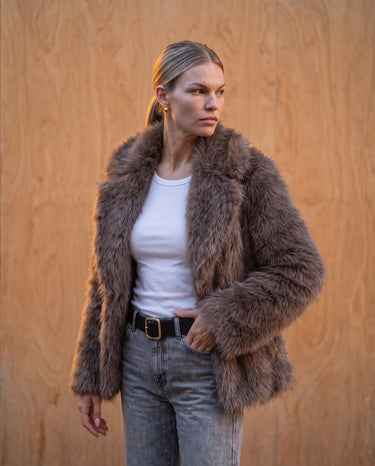 Model wearing the dark brown faux fur Lira Jacket open over a white tank top and blue jeans, front view