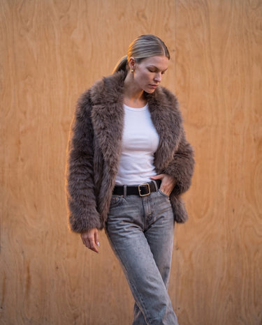 Model in the dark brown faux fur Lira Jacket with hands in pockets, three-quarter front view