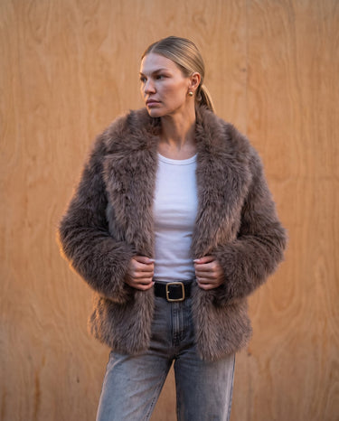 Model standing in the dark brown faux fur Lira Jacket layered over a white tank top and belted jeans