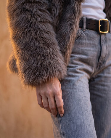 Detail of the Lira Jacket's faux fur sleeve and hip-length hem over blue jeans