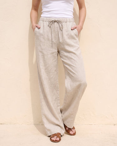 The Loelia Linen Pants in natural linen — wide-leg linen trousers, front view with hands in pockets on model