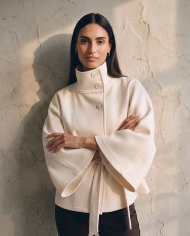 The Lorenne coat in white — front view with arms crossed on model