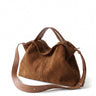 The Manon Suede Tote in tan, three-quarter studio view showing the slouched suede body, leather top handles and adjustable crossbody strap